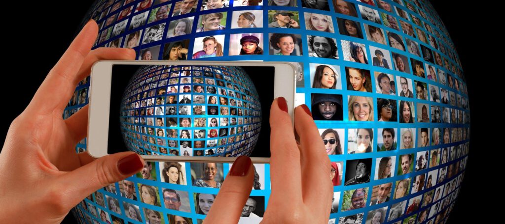Ein Globus mit Gesichtern von Menschen aus aller Welt. Davor ein Smartphone, das ein Bild davon macht.