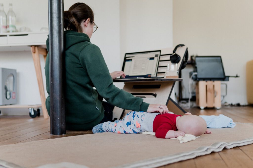 Eine Frau arbeitet am Computer und hutscht gleichzeitig ihr Baby