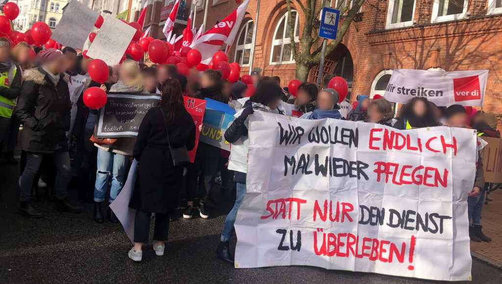 Pflegende auf einem Streik. Auf einem Schild rechts unten steht "Wir wollen einfach mal wieder pflegen, statt nur den Dienst zu überleben"